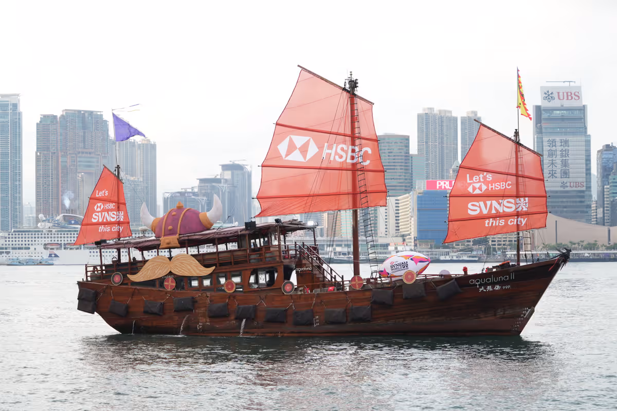 Traditional junk boat in Hong Kong harbor with city skyline.