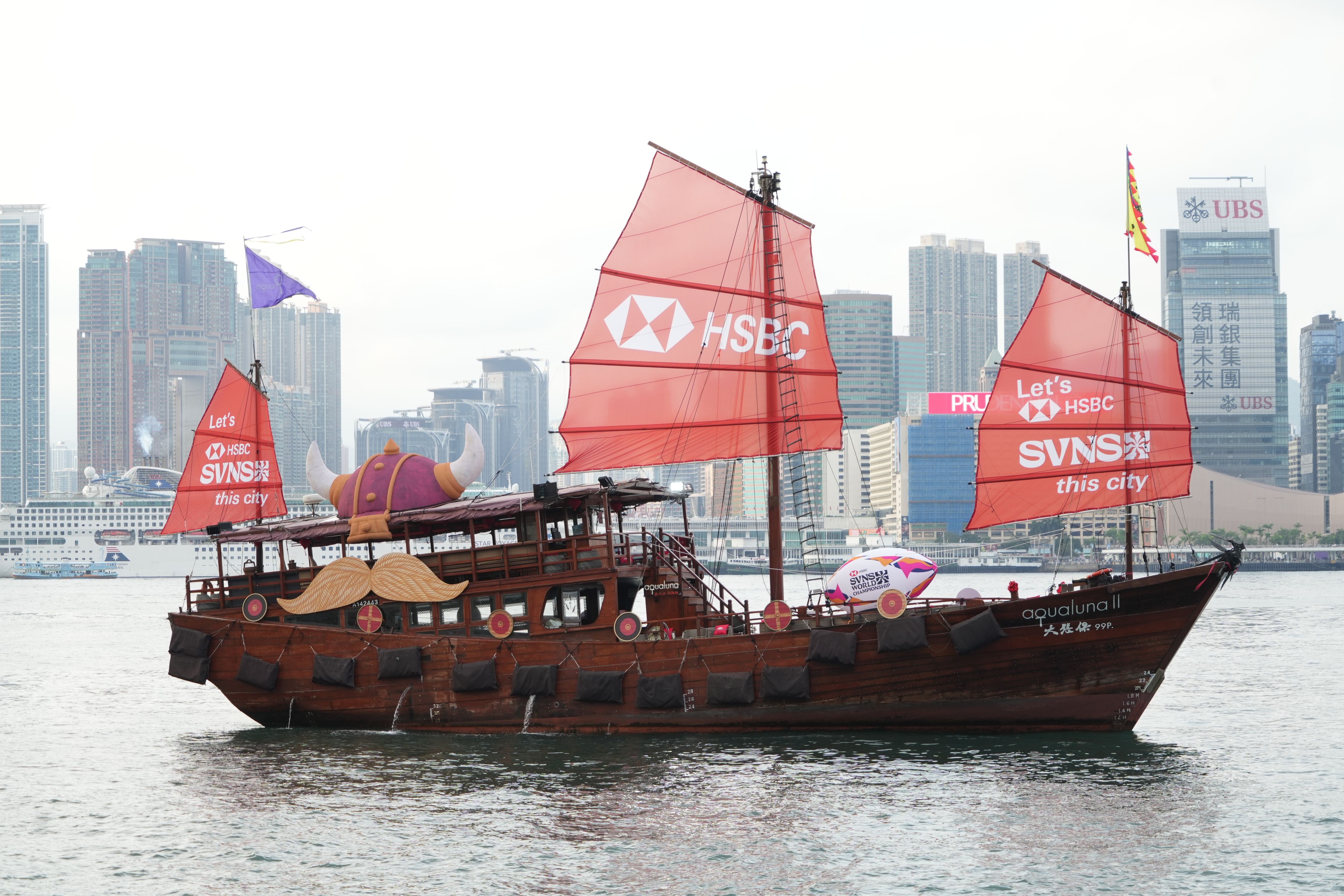 Traditional junk boat in Hong Kong harbor with city skyline.